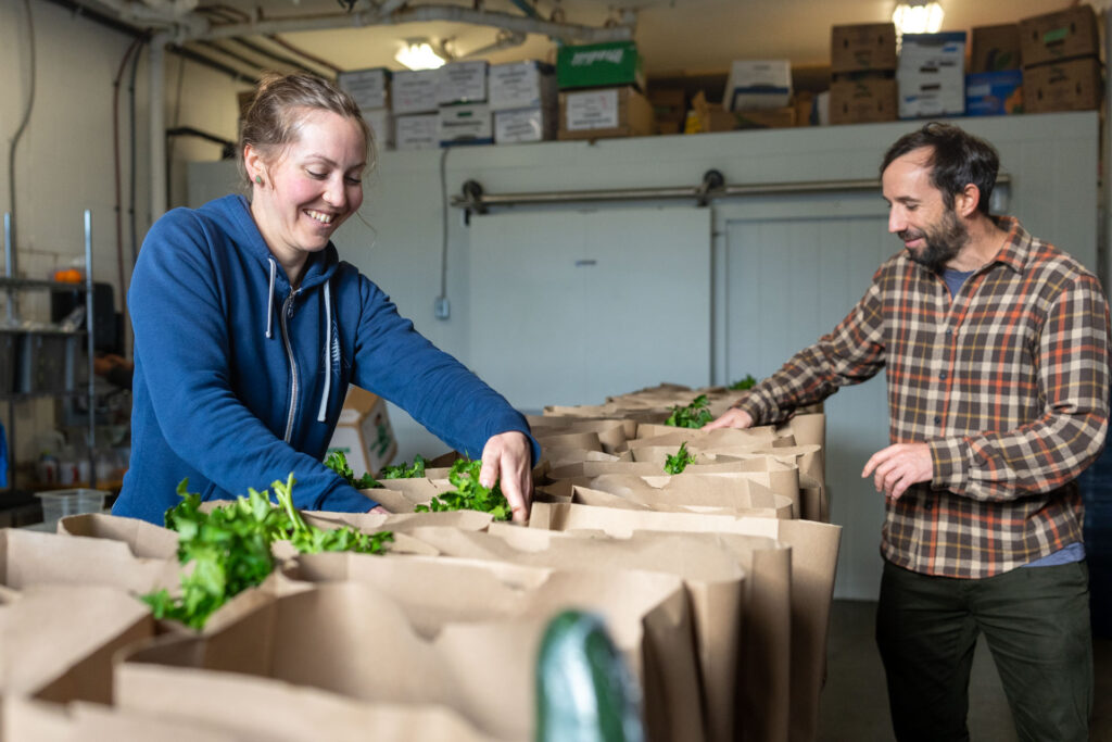 Two LUSH Valley staff members pack a collection of Good Food Boxes with fresh green produce during the busy growing season.
