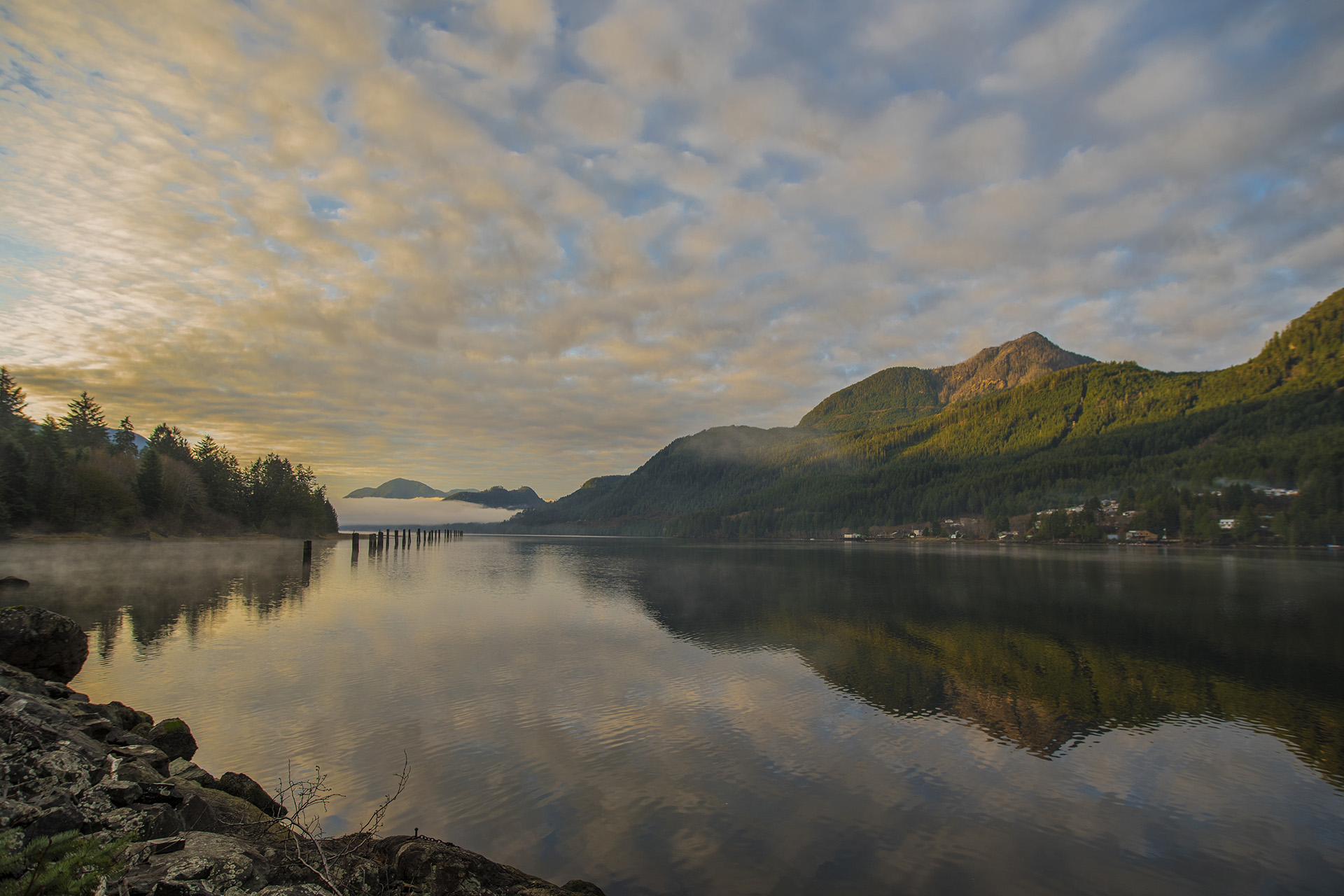A stunning sunrise above the calm water of Tahsis inlet and Nootka Sound. The water is calm, reflecting the large mountain landscape that surrounds the village on the west coast of Vancouver Island.
